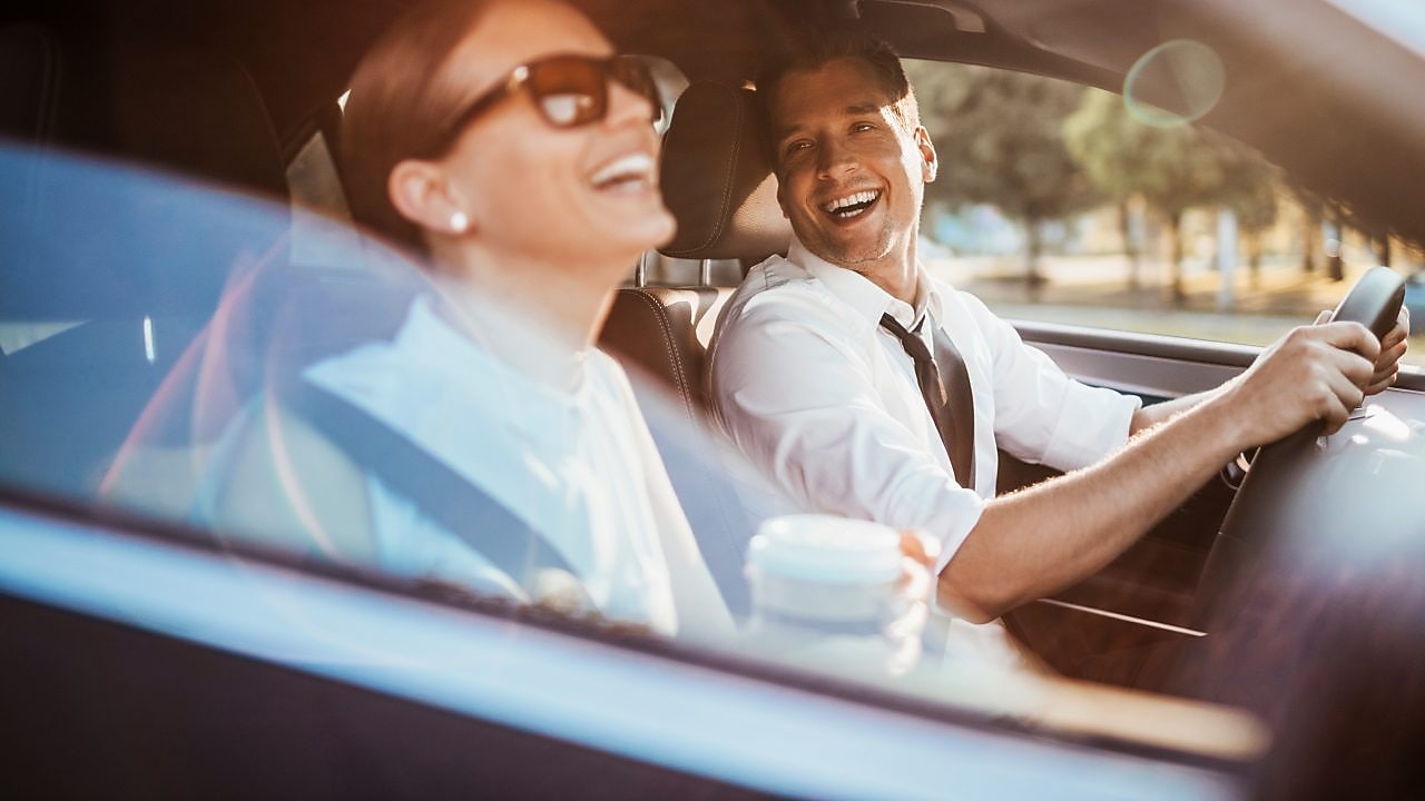 Usměvavý řidič kouká na usměvavou spolujezdkyni se slunečníma brýlema.