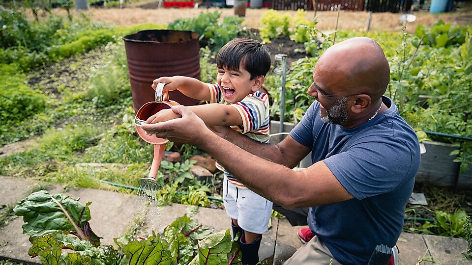 Мъж помага на усмихнато дете да полива цветята в градината