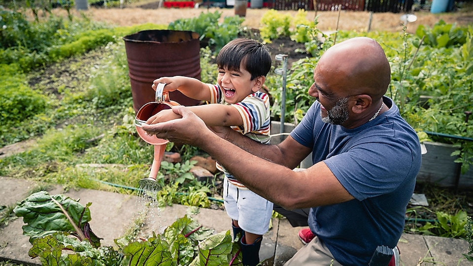 Мъж помага на усмихнато дете да полива цветята в градината